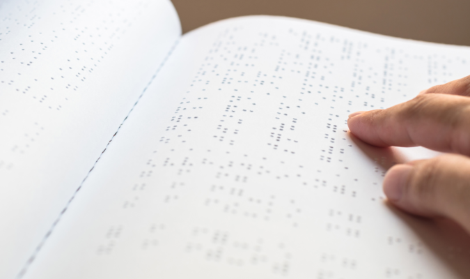 Fotografia di una mano che legge un libro in Braille